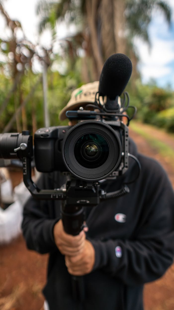 A videographer holding a professional camera and microphone outdoors.